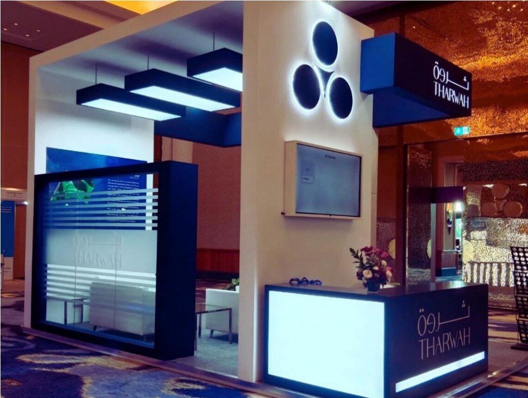 Tharwah exhibition stand by Story Design with the three-circle logo on a backlit tower, a glowing reception counter and suspended light boxes